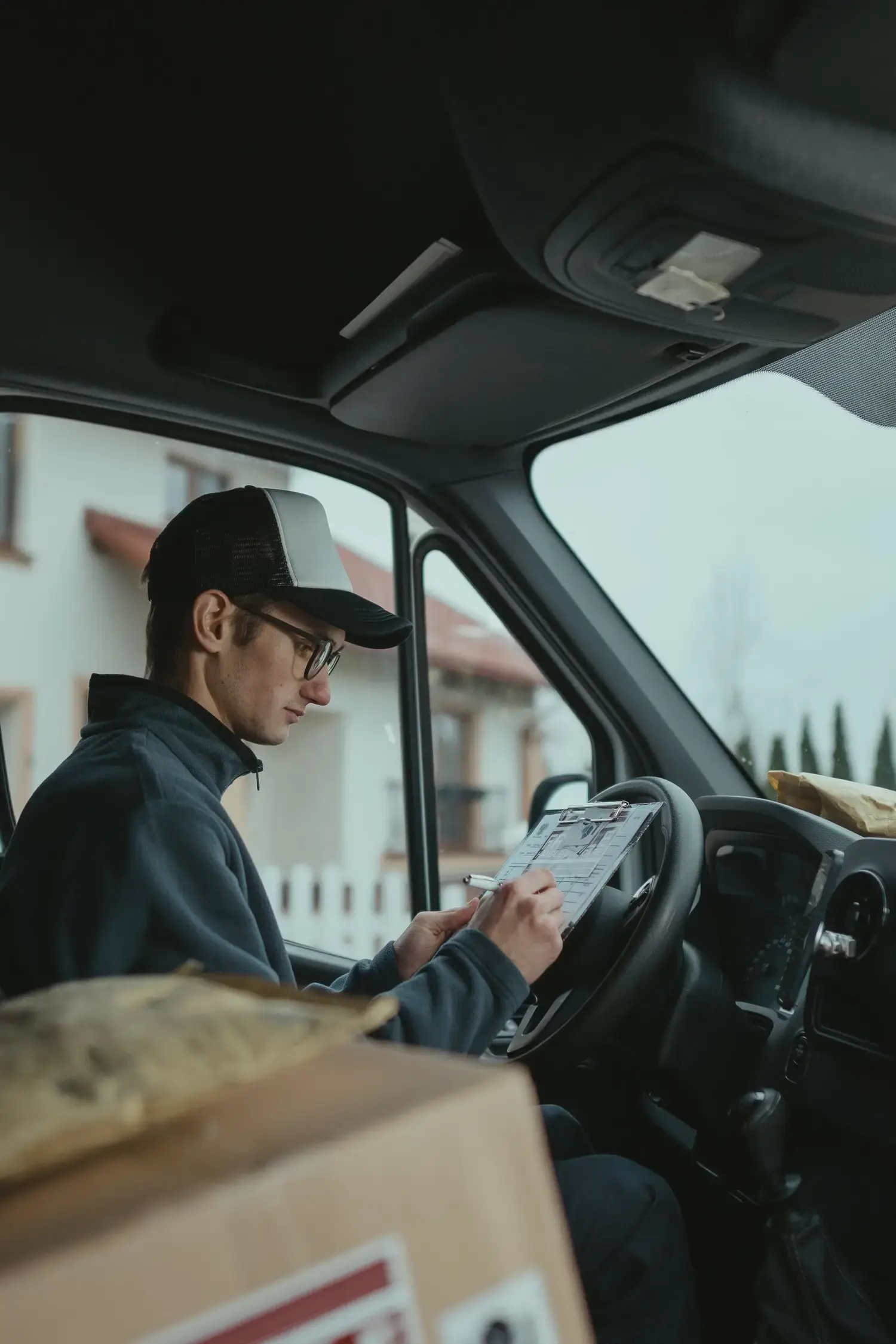 Driver in a vehicle cab completing paperwork on a clipboard