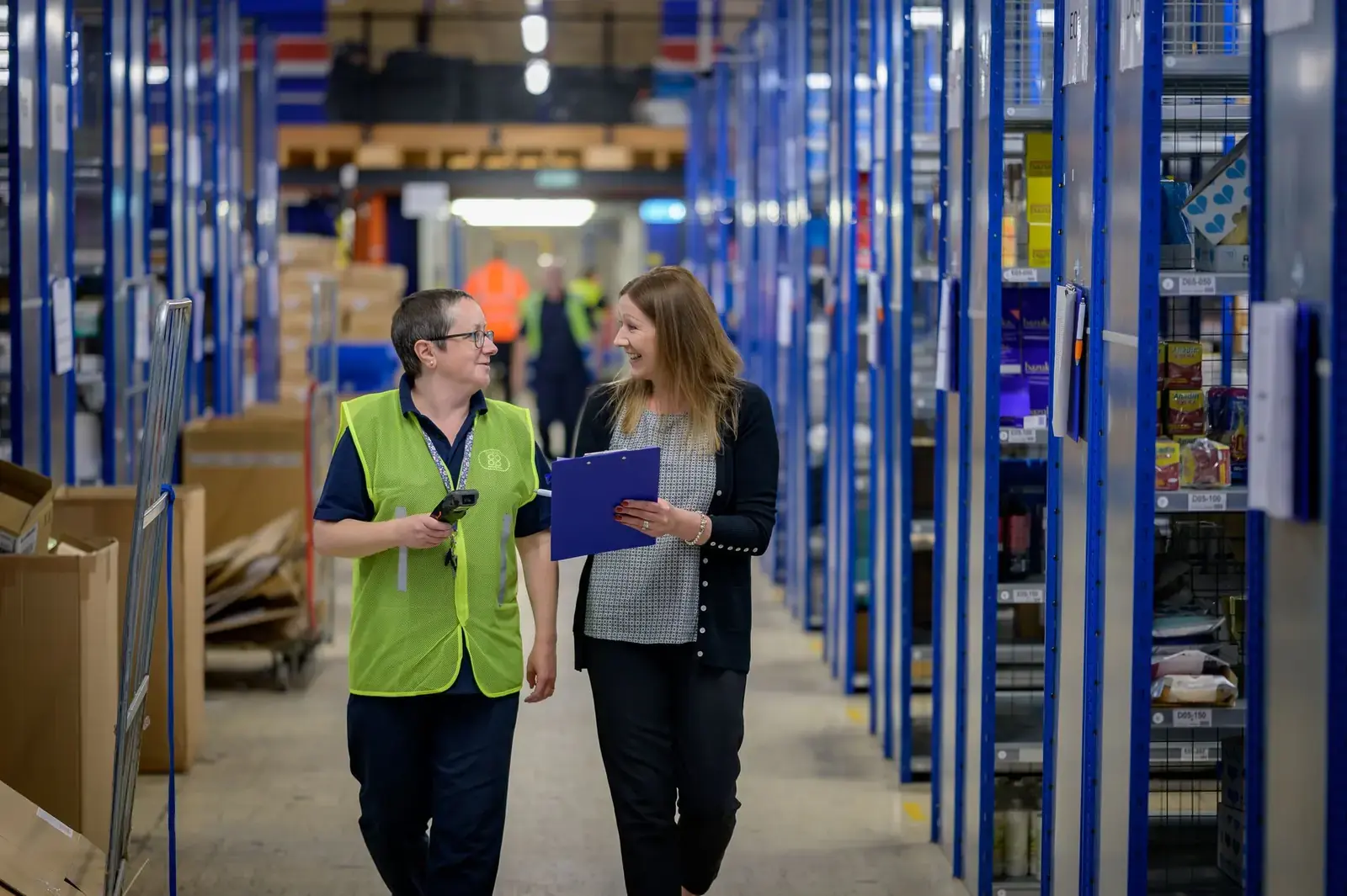 Warehouse operative in a hi-vis vest walking an aisle with a manager holding a clipboard